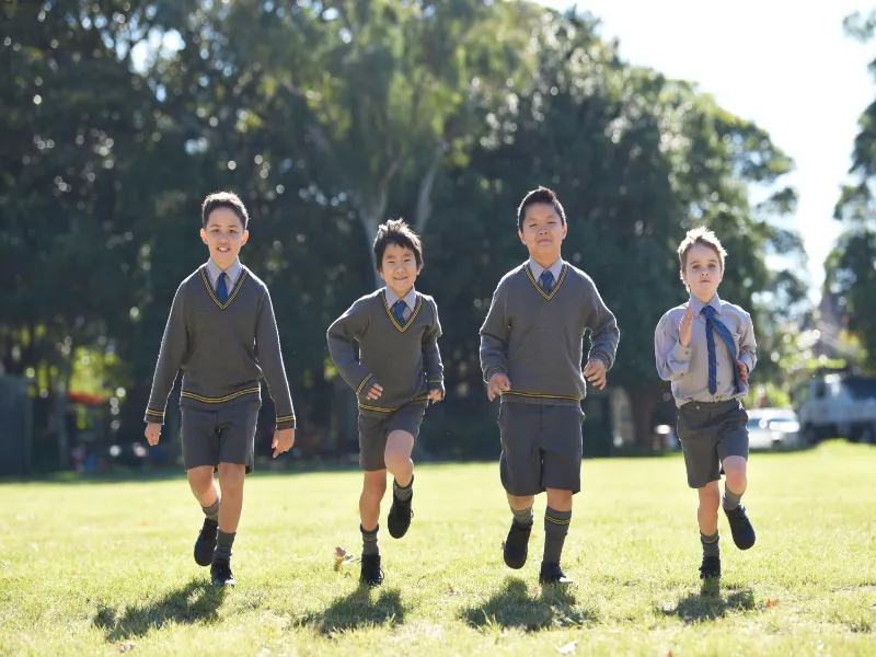 Four Coogee Prep boys running across the sunlit school field