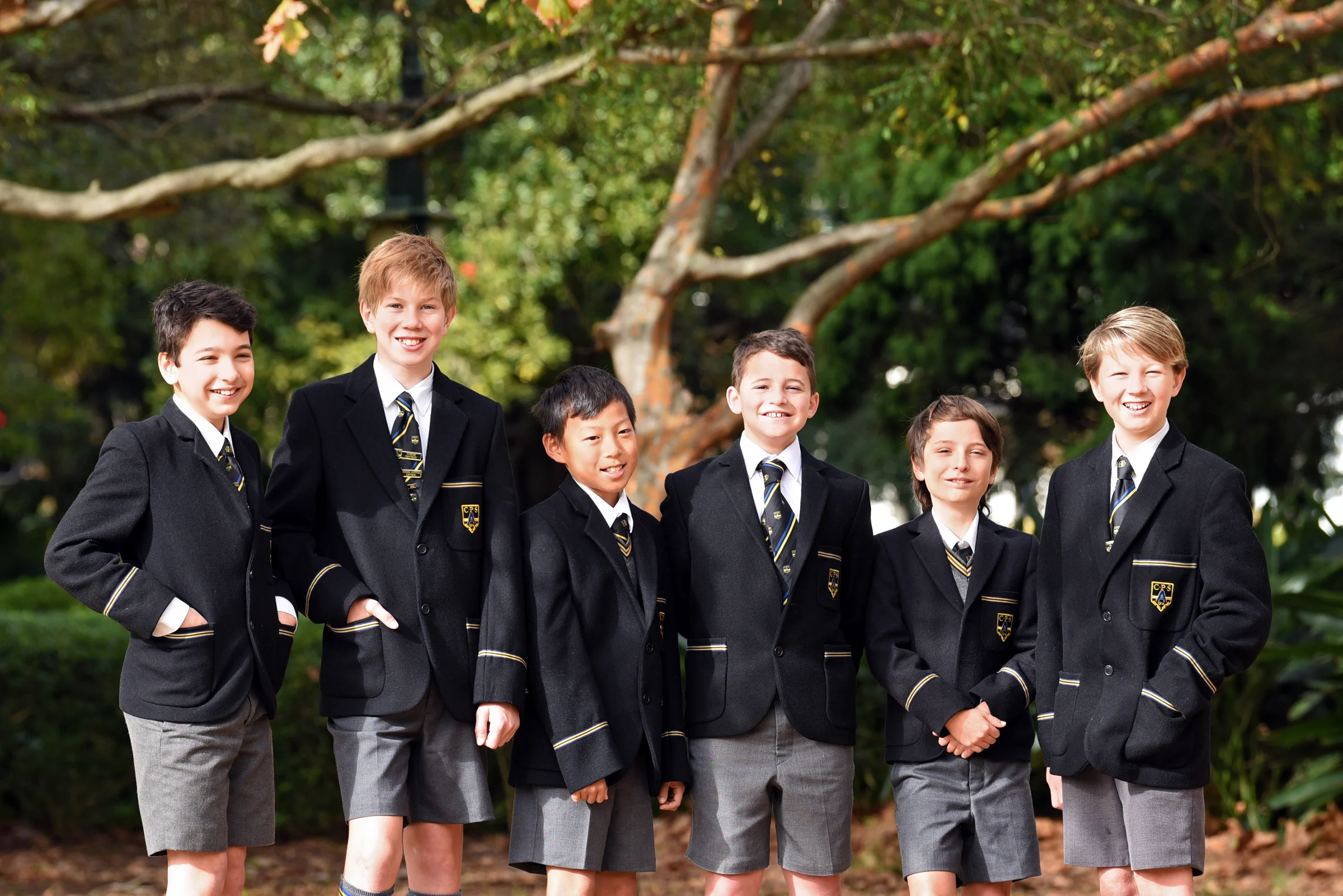 A group of Coogee Prep boys in blazers standing together under a tree