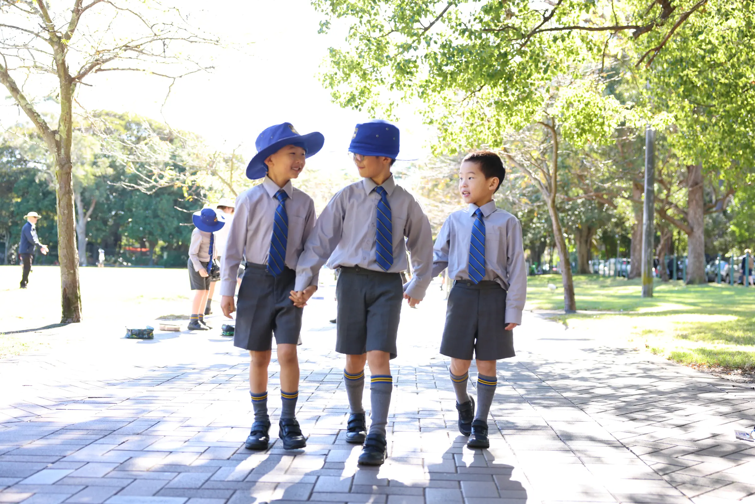 Three Coogee Prep boys in school hats walking together along a path