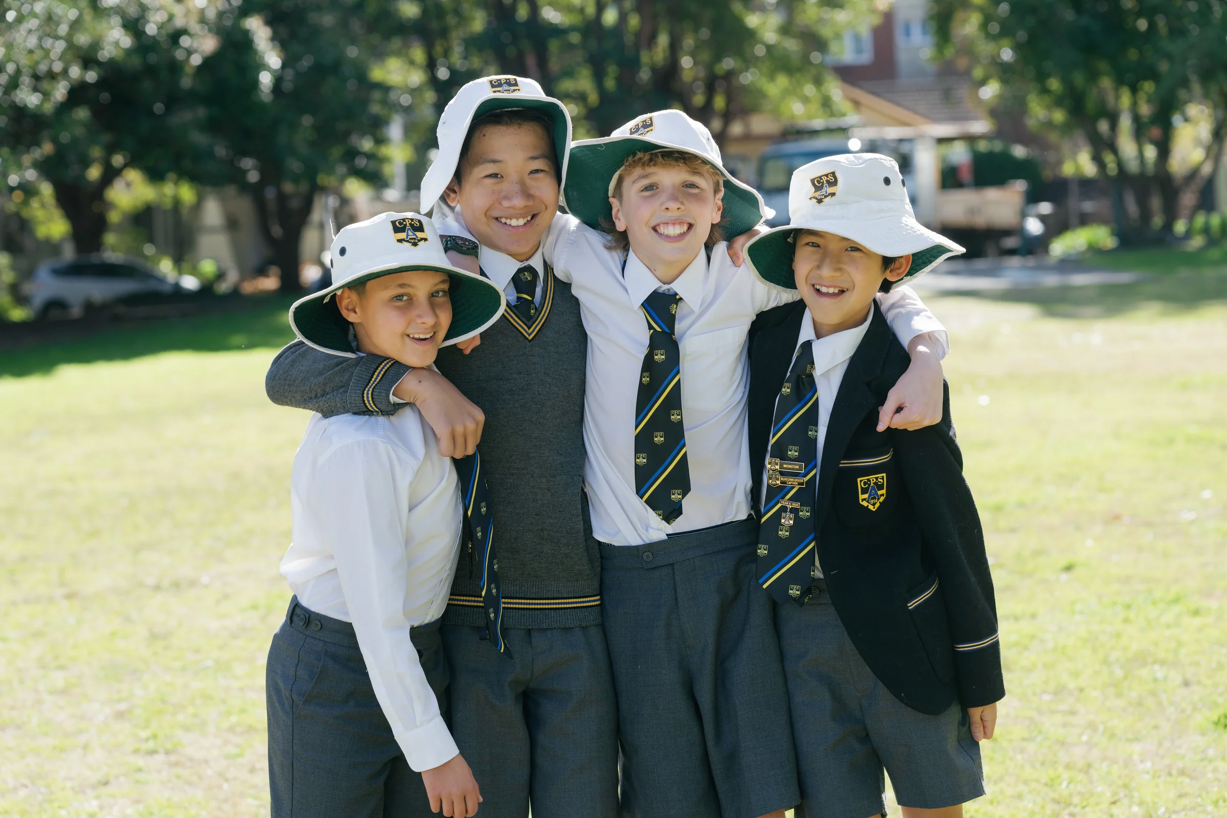 Three Coogee Prep boys in school hats with their arms around each other on the field