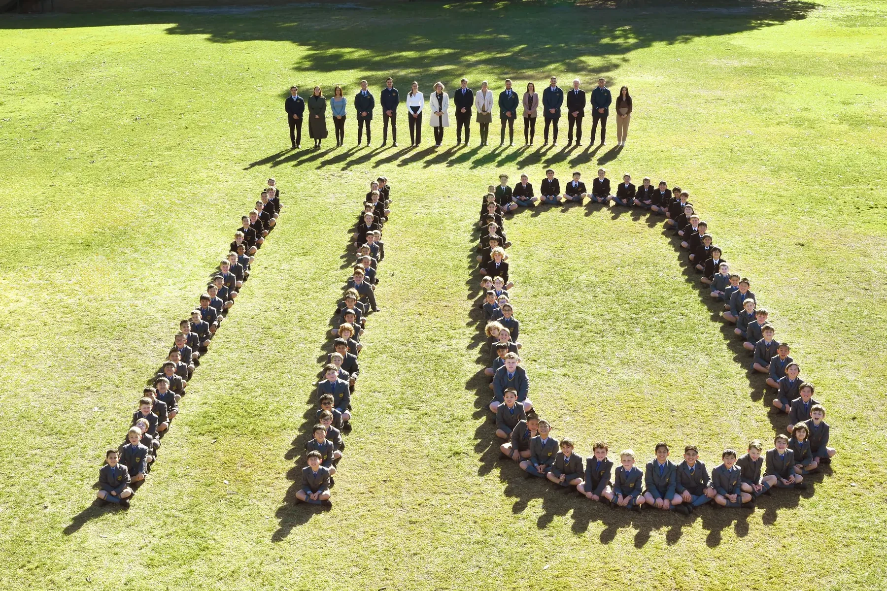 The whole Coogee Prep school standing in formation to spell 110 on the school oval, with the staff behind them